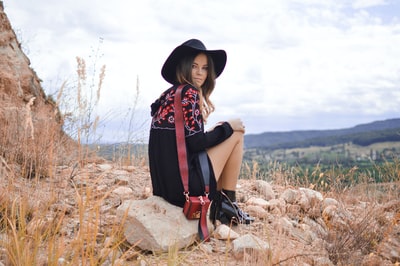 The woman sitting near brown grass gray boulders
